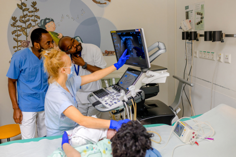 Takondwa Chimowa (li.) und Mubarack Ayamie gemeinsam mit Assistenzärztin Dr. Alena Gschwind bei der Ultraschalluntersuchung eines Neugeborenen. Foto: Rodigast/UKJ