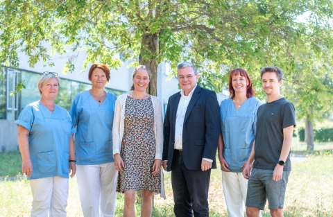 Auf dem Fotos sind die Mitarbeitenden der integrierten Biobank Jena, kurz IBBJ, zu sehen. Sie stehen vor dem Klinikgebäude, das im Hintergrund zu sehen ist. 